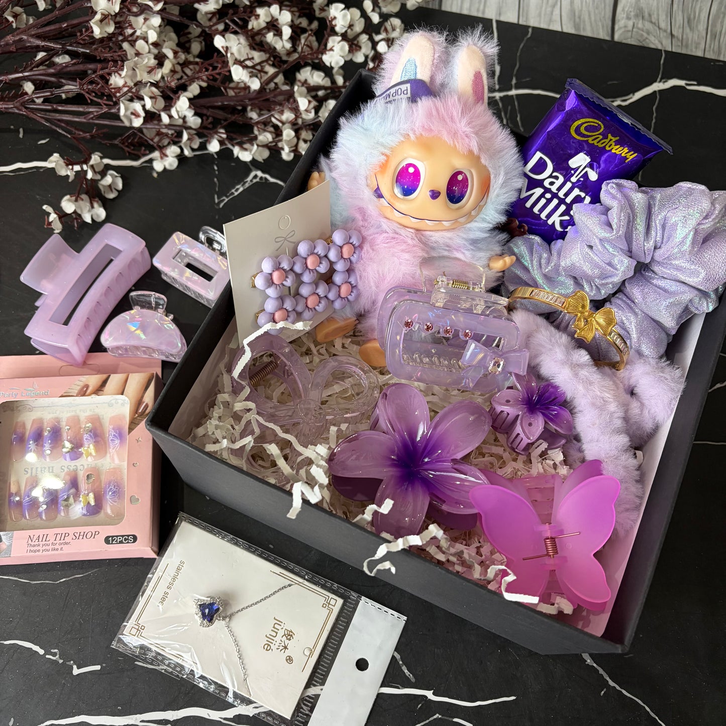 Gift box with a plush toy, candy, and stationery items on a black marble surface.